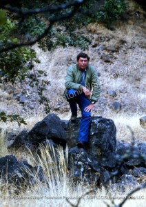 Claude Akins sits on a rock